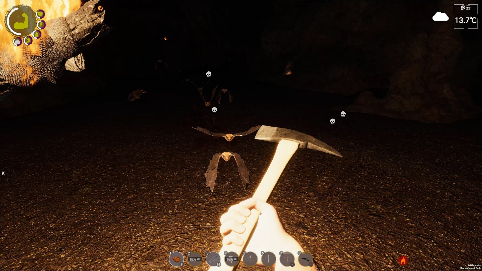 The image shows a first-person perspective inside a dark cave, with the player's hand holding a pickaxe illuminated in the foreground. Several bats with glowing eyes are flying toward the player, their wings spread wide in the dim light. The cave floor is covered in a textured, earthy surface, and small skull icons hover near some of the bats, indicating danger or targets. On the left side, a portion of a large, burning creature or object emits a bright orange flame. The game interface displays item slots and a small map in the top left corner, while a weather widget in the top right shows a temperature of 13.7°C with cloudy conditions.