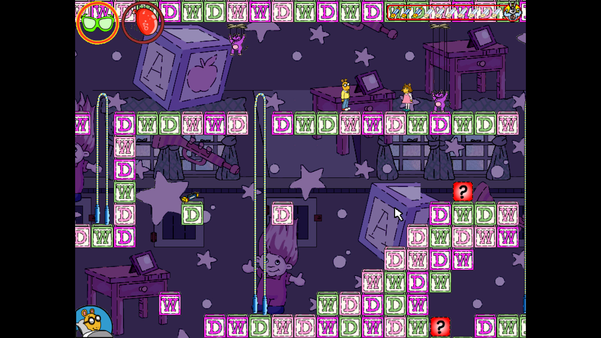 The image shows a colorful, puzzle-style video game screen featuring a dark purple background with stars and circles. The playing field consists of multiple blocks labeled with the letters "D," "W," and "M" in alternating pink and green colors, forming a grid pattern. Various animated characters, including a yellow anthropomorphic character and a girl, stand on some blocks, while other characters resembling puppets hang from strings above desks with computer monitors. Large toy-like objects such as building blocks and a telescope are scattered in the background, giving the scene a whimsical, playful atmosphere. Two red blocks with question marks are also visible among the lettered blocks.