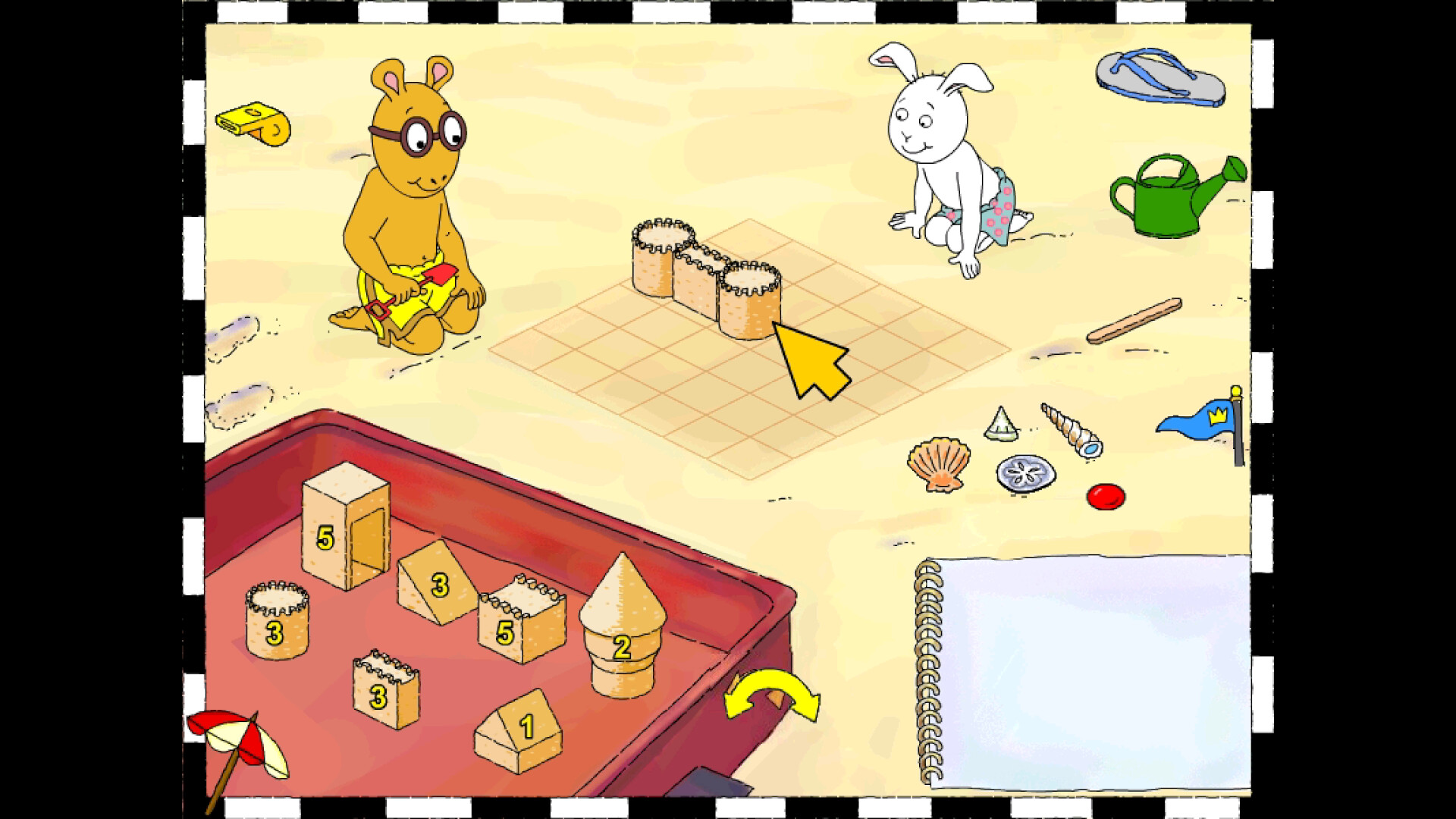 The image shows an animated beach scene featuring two cartoon characters-a yellow bear-like figure wearing round glasses and yellow swim shorts, and a white rabbit in pink polka-dot swim trunks. Both characters are sitting in the sand, with the bear holding a small red shovel. In front of them is a grid drawn on the sand where three cylindrical sand towers are built side by side. To the left, there is a red container holding various sandcastle pieces numbered 1, 2, 3, and 5, shaped like cubes, cones, and walls. Various beach items, including a yellow whistle, a green watering can, a blue flip-flop, several seashells, a red button, a small blue flag with a crown emblem, and a stick, are scattered around the sandy area. A spiral-bound notebook lies open at the bottom right corner of the scene.