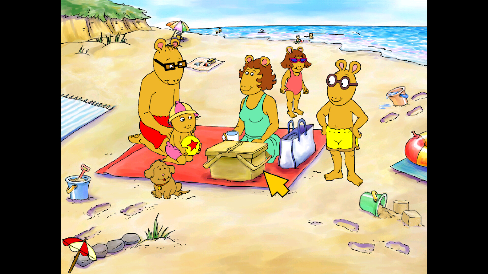 The image depicts an animated family of anthropomorphic aardvarks enjoying a day at the beach. They are sitting and standing on the sandy shore near the ocean, with beach toys such as buckets, shovels, and an inflatable ball scattered around. A red blanket is spread on the sand where three family members are seated; an adult male wearing red swim trunks and glasses, a baby in a pink hat holding a yellow and red ball, and an adult female in a turquoise swimsuit holding a cup. Nearby, a small brown dog sits contentedly on the sand. Another child wearing a pink swimsuit and purple sunglasses walks toward the water, while an older child in yellow swim trunks and round glasses stands with hands on hips, smiling. The background shows a cliff with greenery and a few umbrellas and beach towels further along the shore.