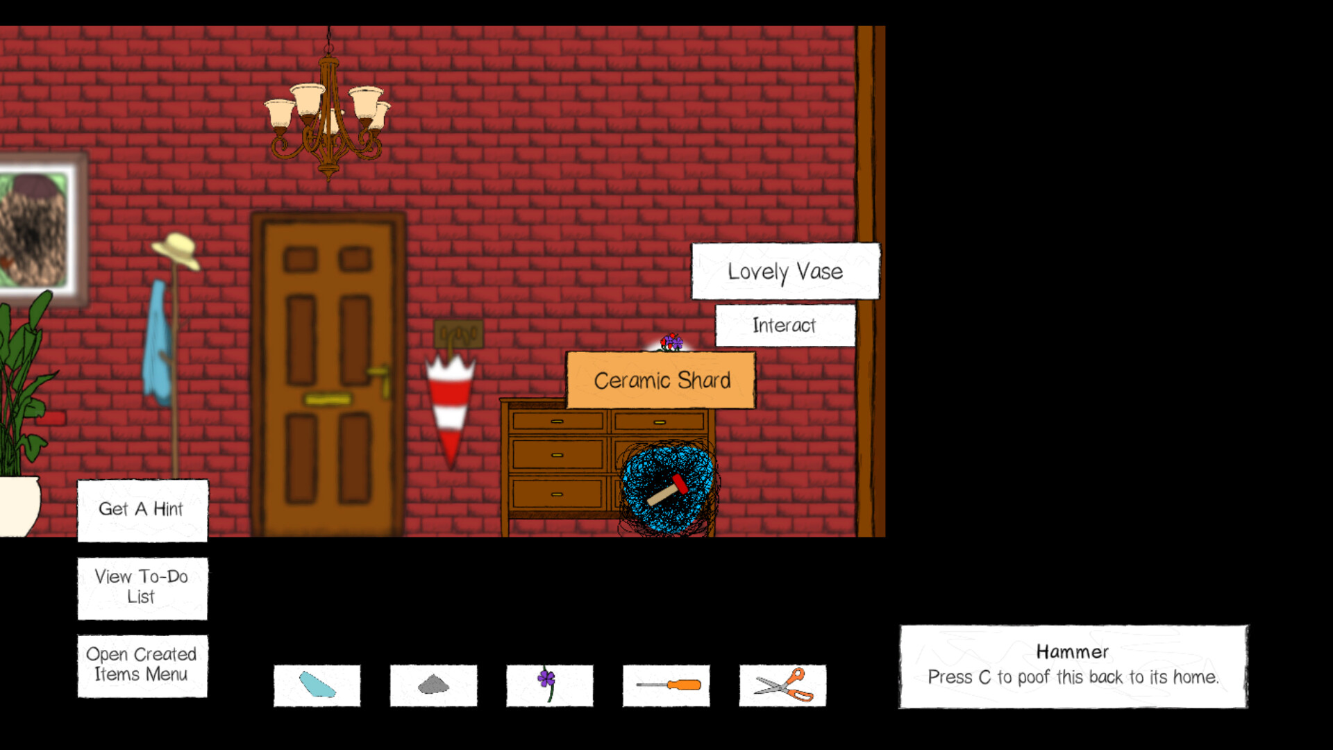 The image shows a cozy room with red brick walls, a wooden door at the center, and a chandelier hanging from the ceiling. To the left of the door is a coat rack with a hat and a blue jacket, and to the right is a small wooden dresser with multiple drawers. On top of the dresser, a broken "Lovely Vase" piece called "Ceramic Shard" is highlighted with an option to "Interact," and a small hammer is visible next to it. At the bottom of the screen, there are menu options including "Get A Hint," "View To-Do List," and "Open Created Items Menu," along with inventory icons representing various items, including a hammer with a prompt instructing players to press "C" to return it to its place.