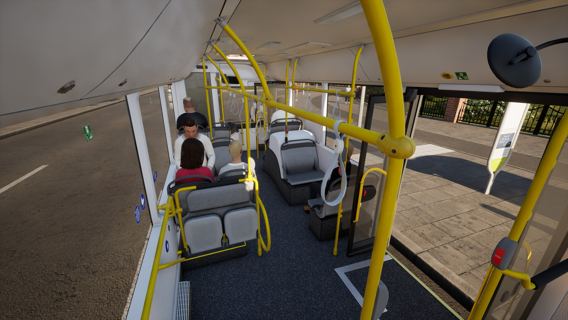 The image shows the interior of a public bus viewed from the middle toward the front. There are yellow handrails running along the ceiling and sides, with several white hanging straps for standing passengers to hold onto. Four passengers are seated, two of whom are facing forward on the left side, while the other two face opposite directions near the front. The bus doors on the right side are open, revealing a paved sidewalk and a bus stop shelter outside. The interior has gray and black seating with a clean, modern design.