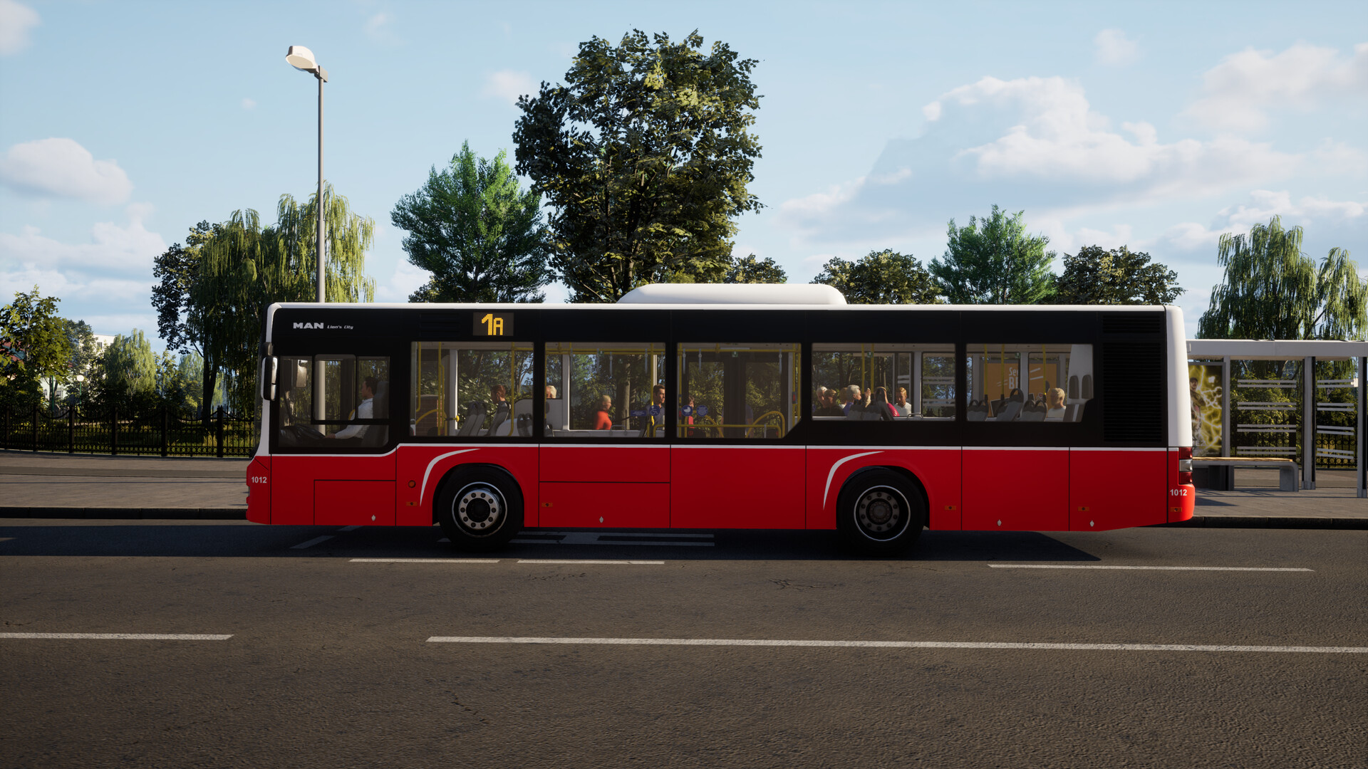The image shows a red and white city bus stopped at a bus stop on a sunny day. The bus is mostly red on the bottom half, with a black and white upper section, and the route number "1A" is displayed on the front. Through the large windows, several passengers are visible sitting inside, and a bus driver is seated at the front. In the background, there are green trees and a clear blue sky with scattered clouds, as well as a bus shelter with benches and some signage.