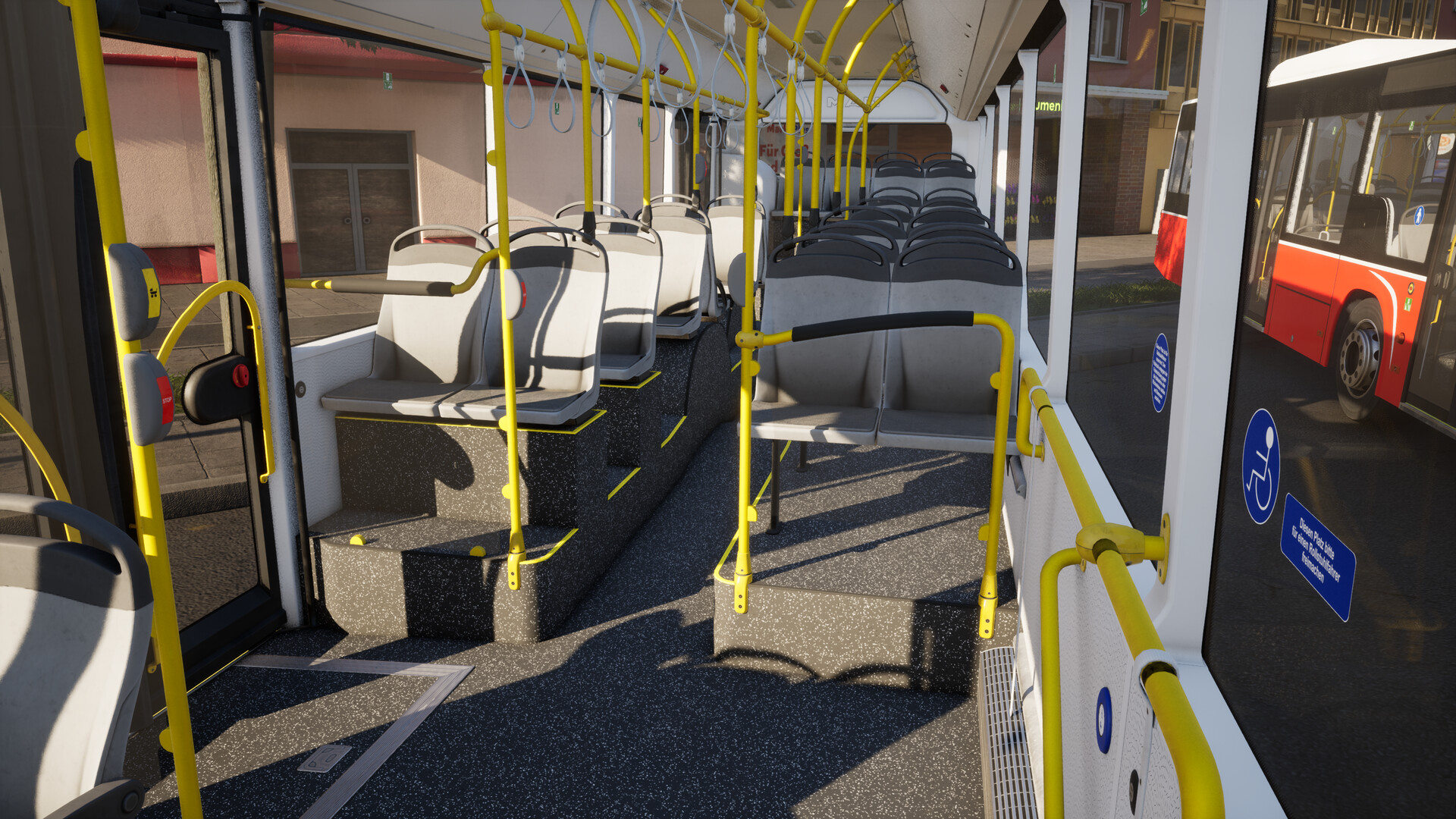 The image shows the interior of a public bus, focusing on the seating area near the front door. There are rows of gray seats with black handrails above them, and bright yellow poles and handles are positioned throughout the bus for passenger support. The floor is dark with a speckled pattern, and sunlight casts shadows inside the bus. Through the windows, another red and white bus is visible parked outside, along with a building in the background. Blue signs indicating priority seating for disabled passengers are displayed on the windows.
