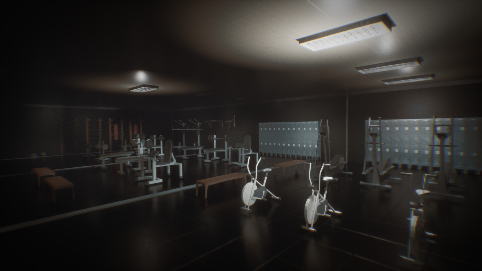 The image shows a dimly lit gym interior with various workout equipment arranged throughout the room. In the foreground, there are two stationary exercise bikes and a wooden bench. Further back, multiple weightlifting machines, benches, and racks with barbells are positioned near the walls, which also feature rows of lockers. The ceiling has rectangular fluorescent lights that cast a soft glow over the dark flooring and walls, creating a somewhat muted and quiet atmosphere.