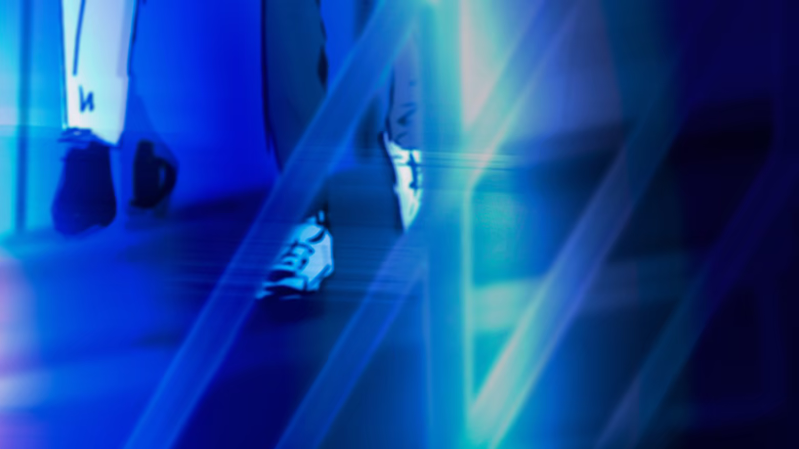 Two people walking down the stairs of a music club, shrouded in neon blue lights.